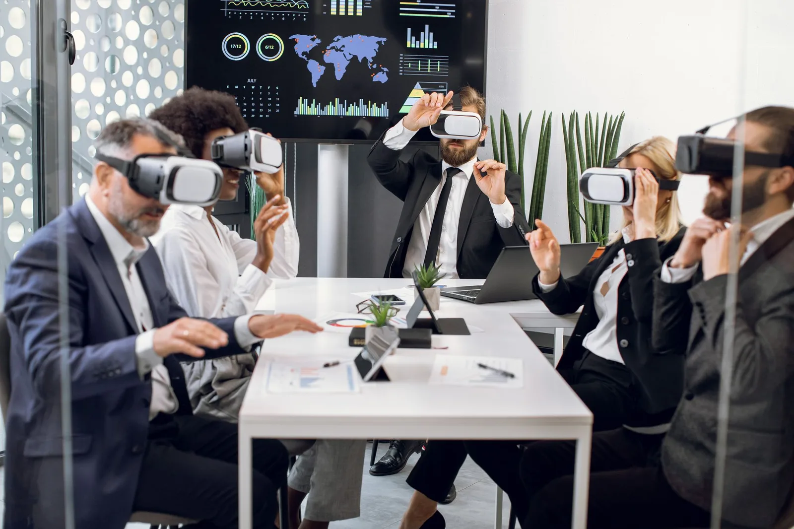 Team wearing VR headsets around a boardroom table with a data dashboard on the wall screen