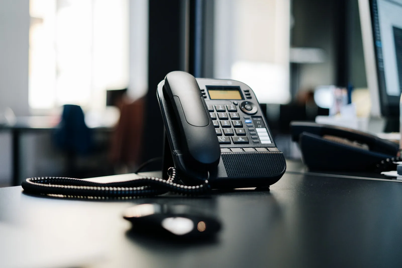 Desk telephone on an office desk with the workspace blurred behind