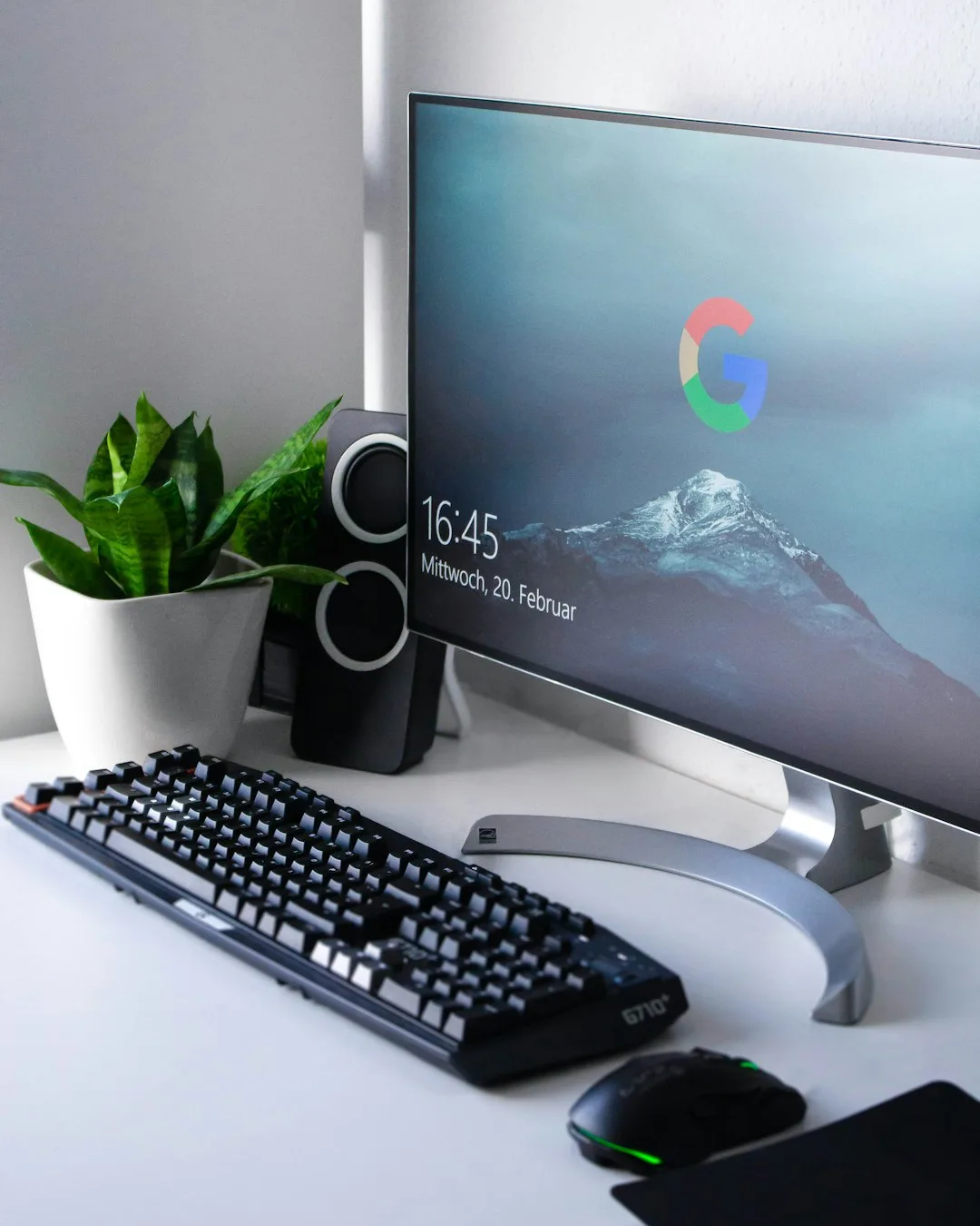 Desk with a widescreen monitor showing the Google homepage, a keyboard, mouse and a plant