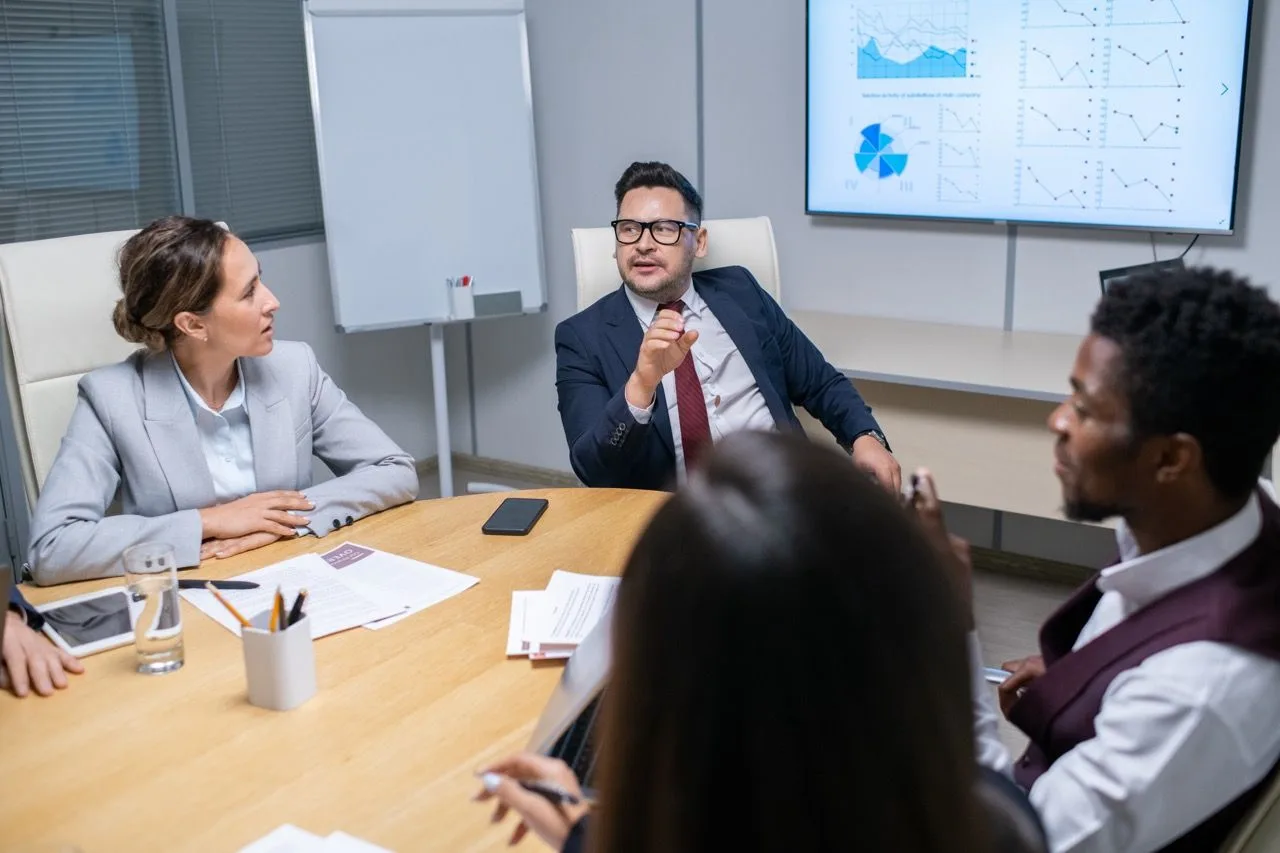 Colleagues meeting around a conference table with charts shown on a wall display