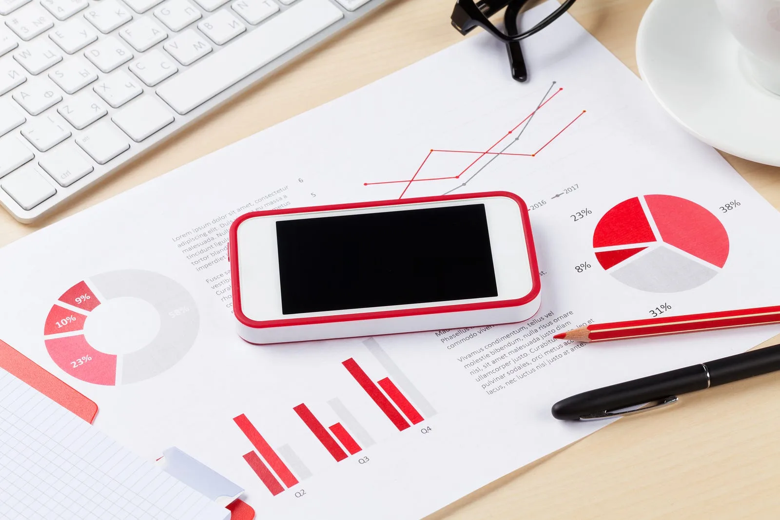 Printed charts and graphs on a desk beside a phone, pen and keyboard