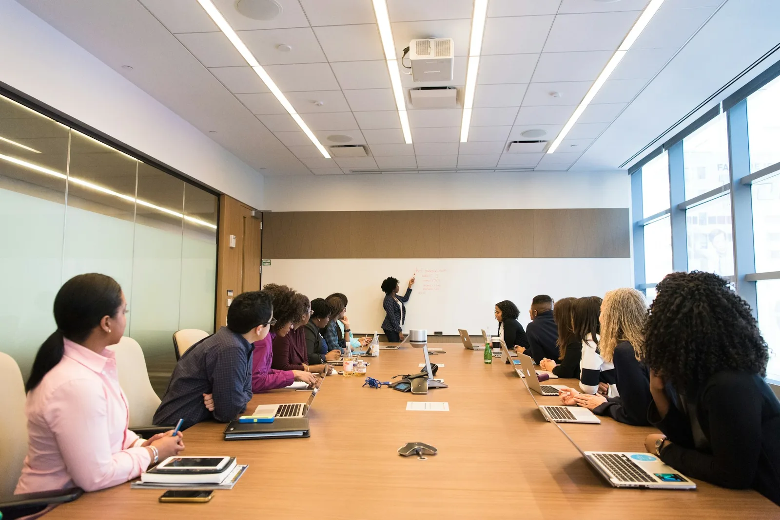 Team seated around a long boardroom table while a colleague presents at a whiteboard