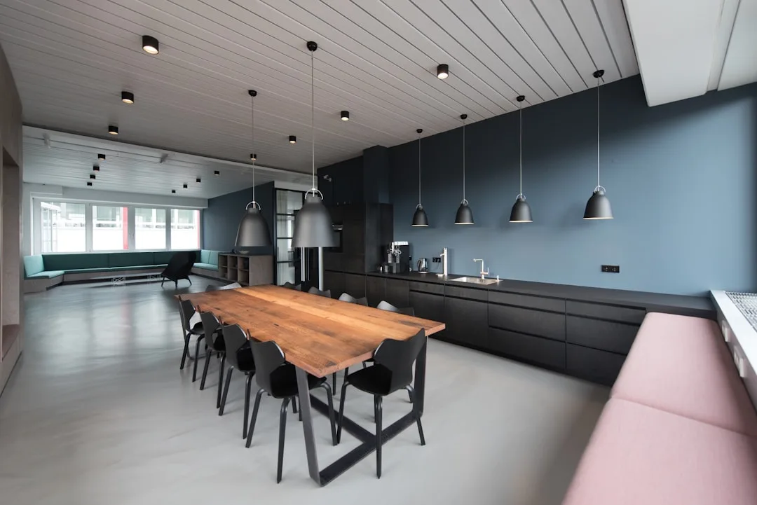 Modern meeting space with a long wooden table, pendant lights and a kitchen counter