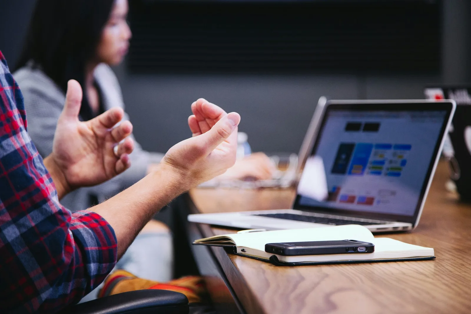 Person gesturing while talking in a meeting, with a laptop open on the table