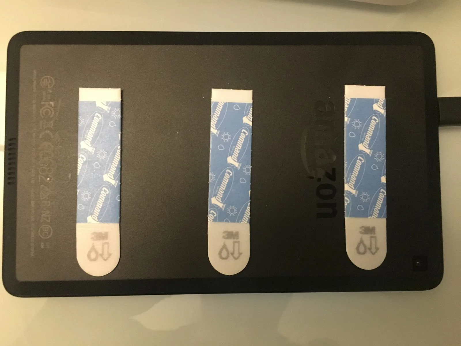 Back of a Fire tablet with three Command adhesive strips applied ready for mounting