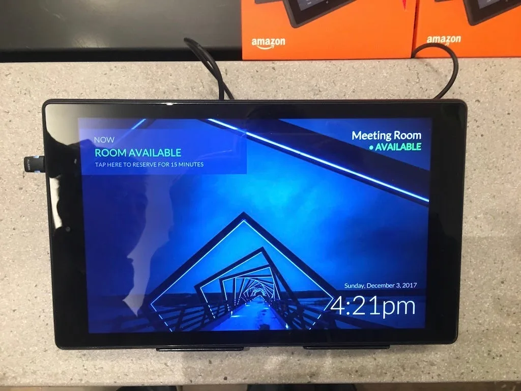 Amazon Fire tablet on a desk showing the meeting room display with the room available