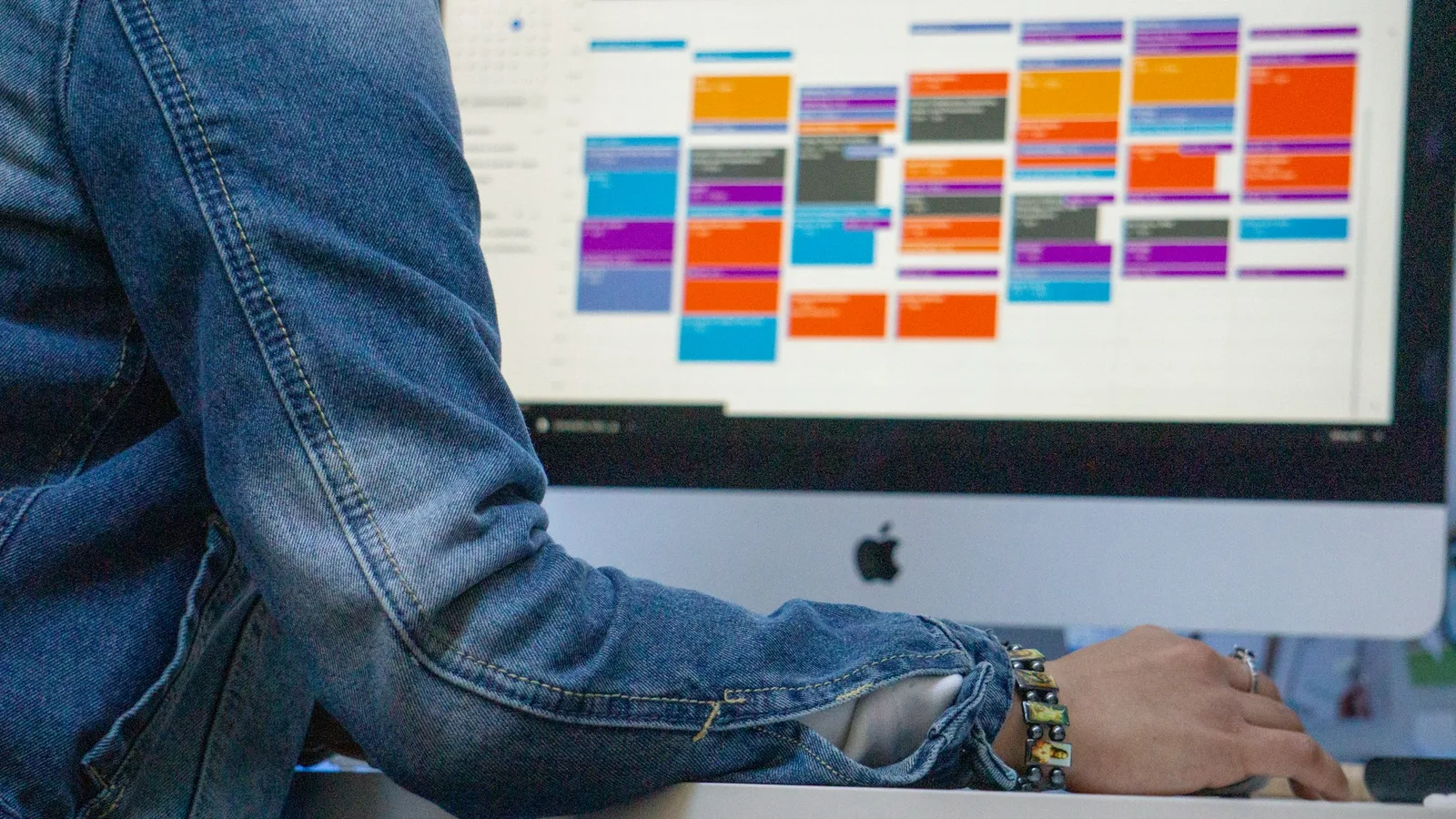 Person at an iMac showing a week view packed with colour coded calendar events