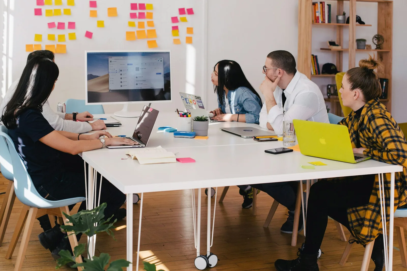 Team meeting around a white table with a wall of sticky notes behind them
