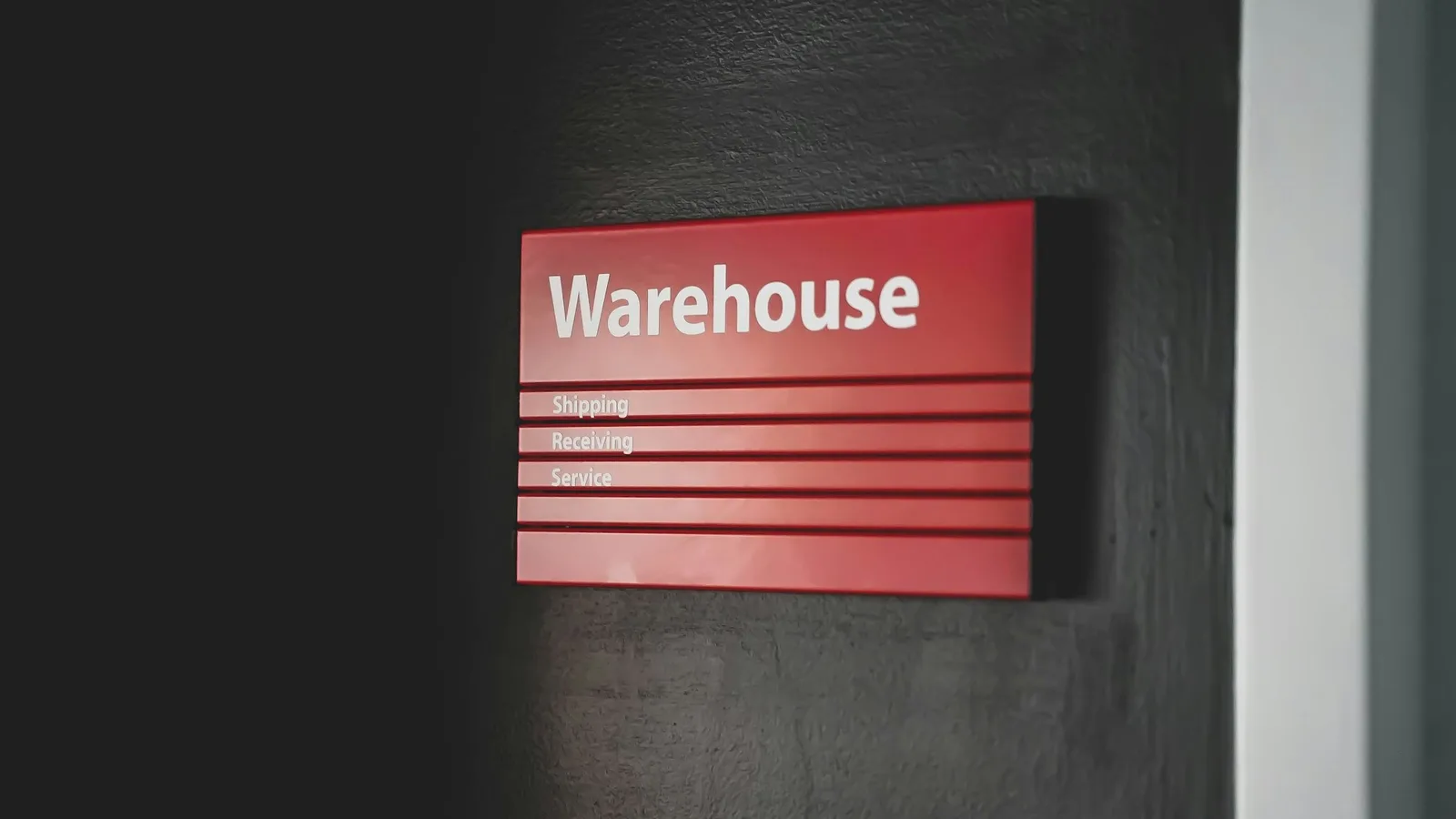 Red Warehouse wayfinding sign on a dark wall listing shipping, receiving and service