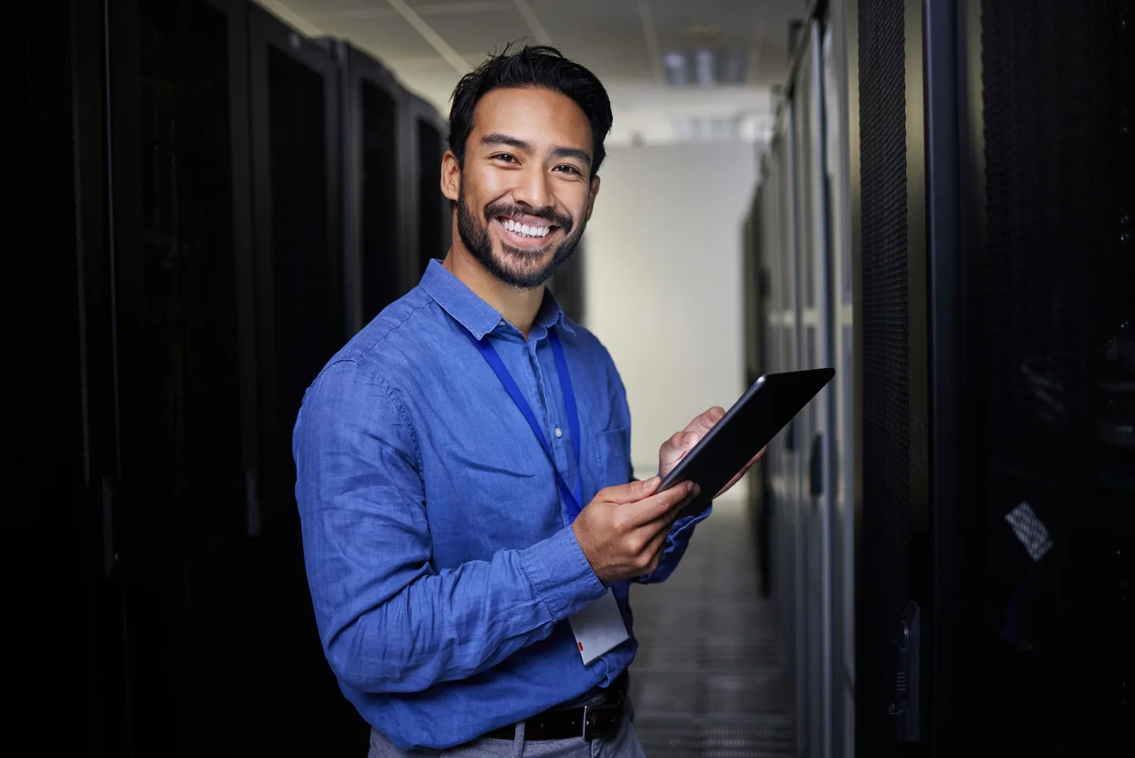 Smiling IT administrator holding a tablet in a data centre aisle