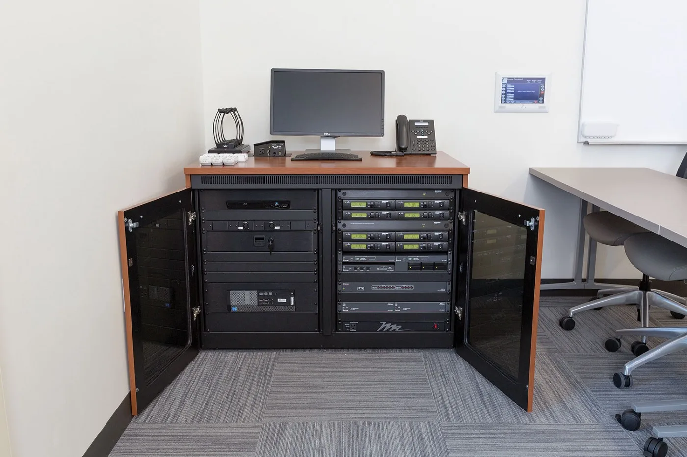 Open audio visual equipment rack cabinet beside a meeting room desk