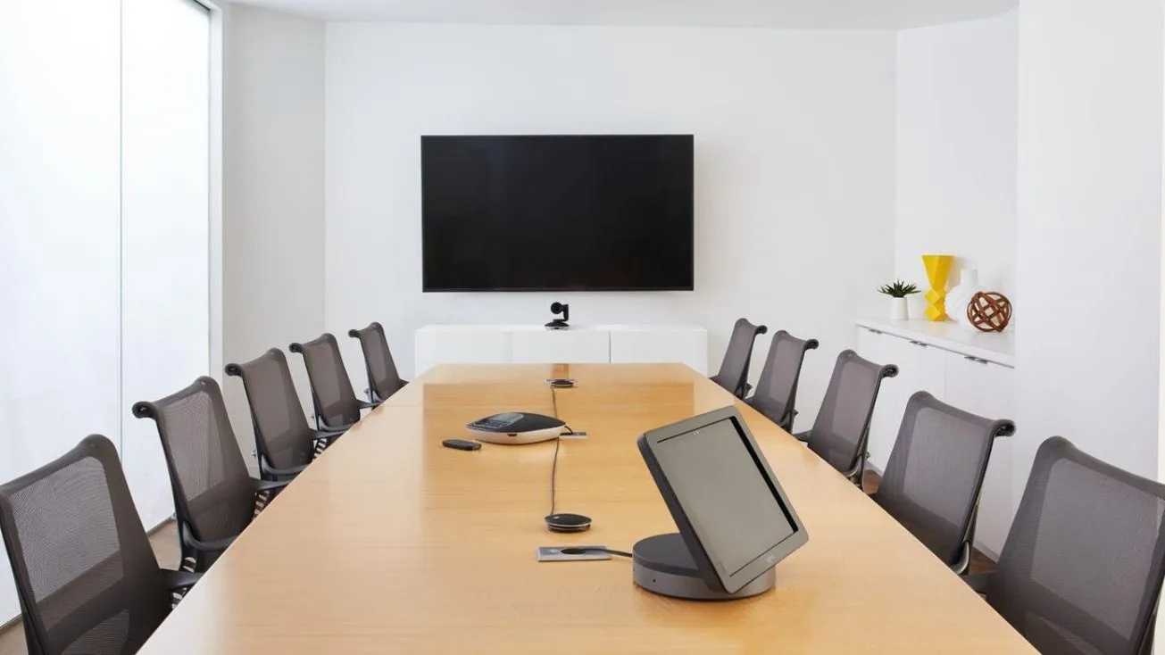 Empty boardroom with a wall mounted display, camera and conference speakerphone on the table