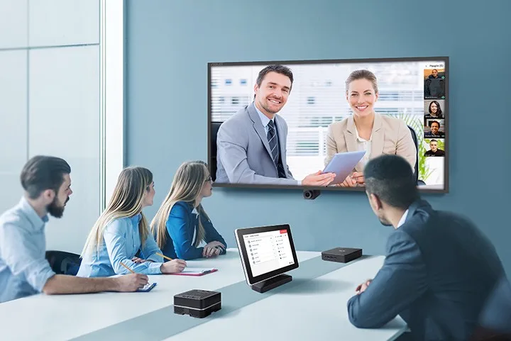 Colleagues in a meeting room joining a video call shown on a wall display